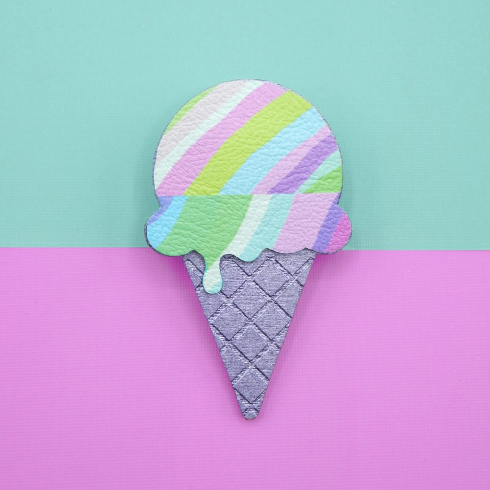 Pastel ice cream brooch with a drippy scoop design in soft lilac, mint, and pink stripes, paired with a textured metallic purple cone. A playful and colourful accessory, photographed against a split mint green and pink background.