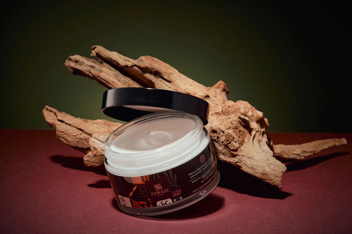 Jar of Pink Prestige whipped natural shea butter on display next to wood, showcasing its smooth, white color