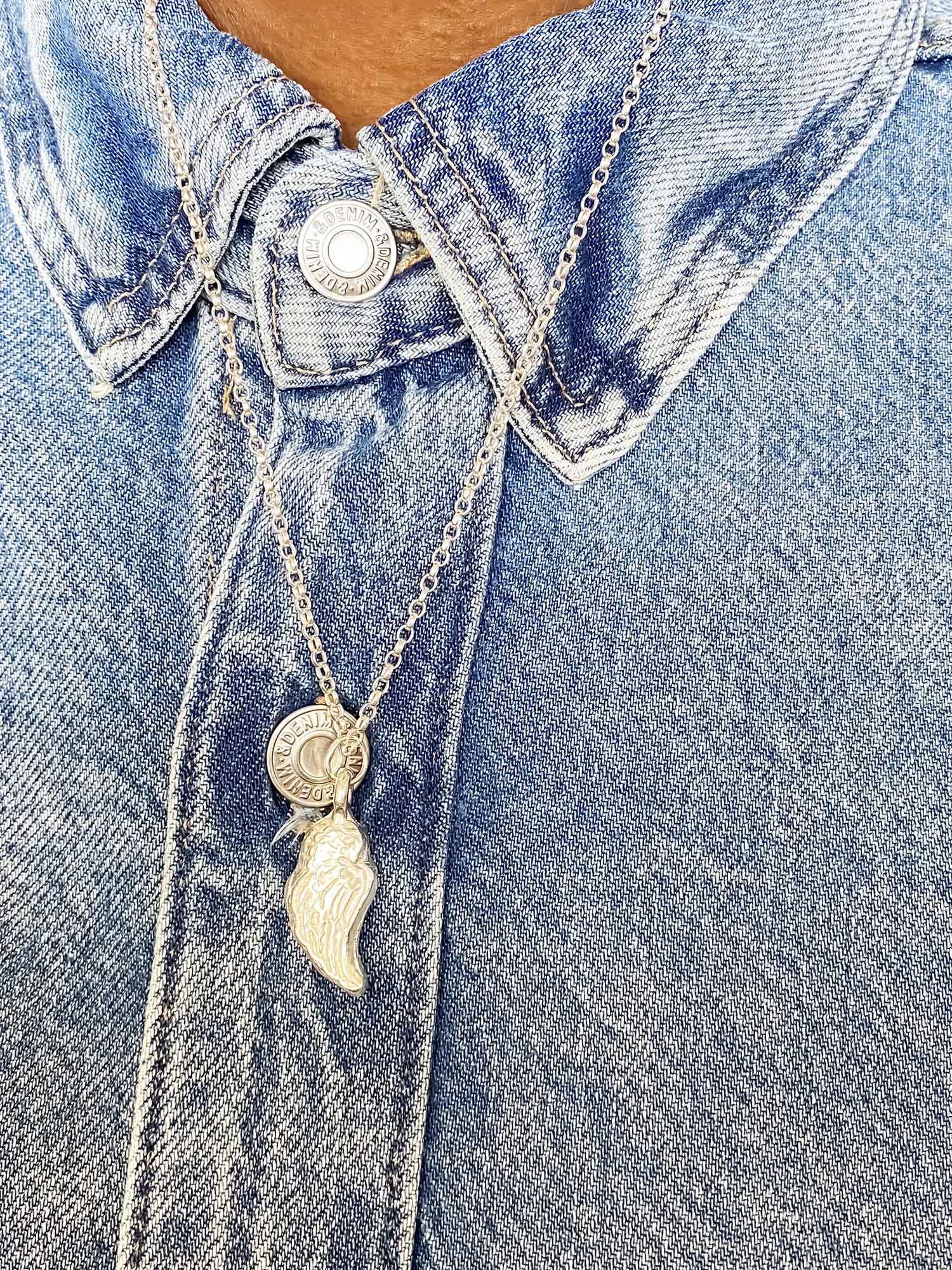 Angel wing pendant necklace worn over a denim shirt