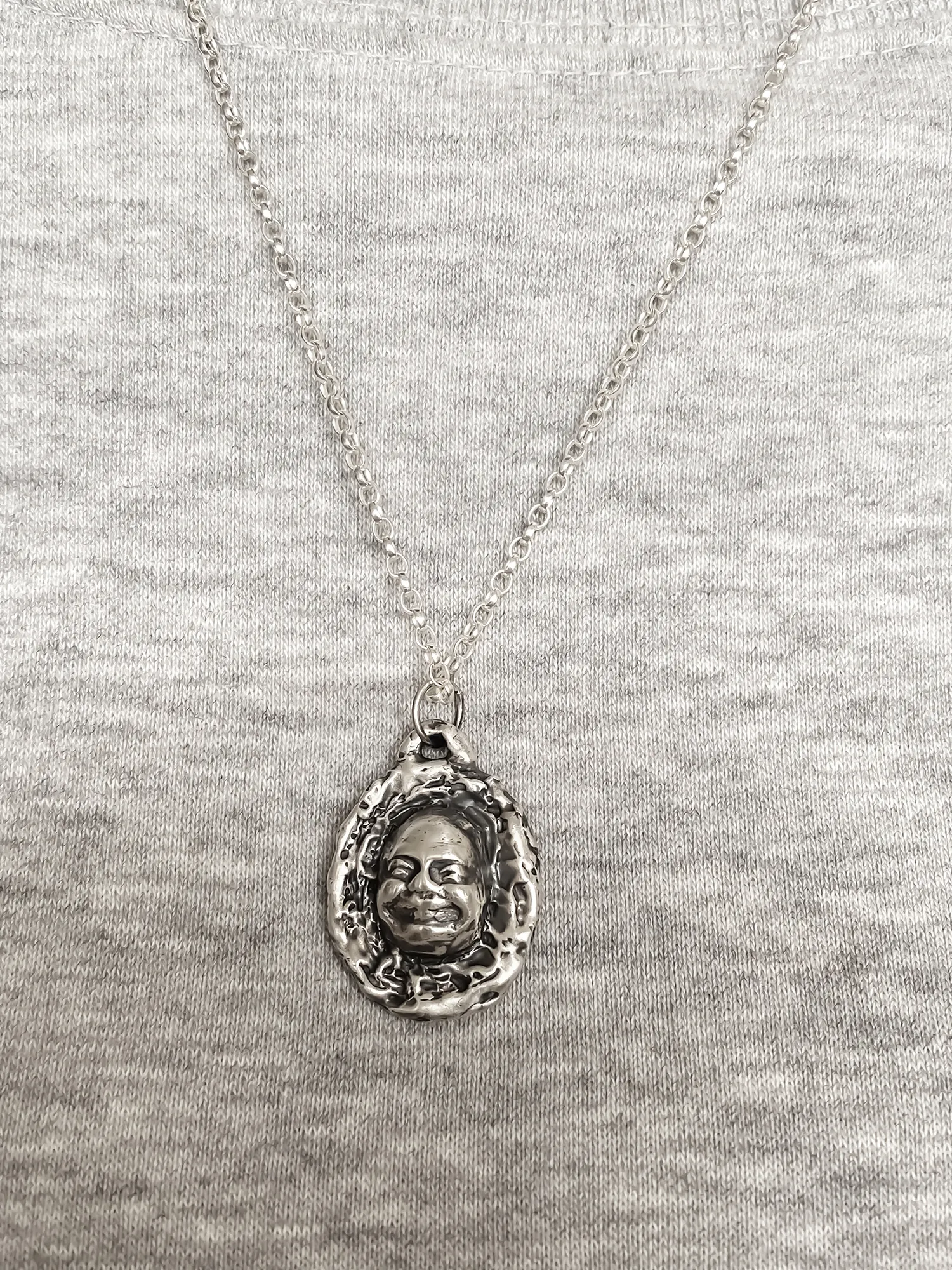 Buddha Face Pendant worn on chest over grey top, close-up