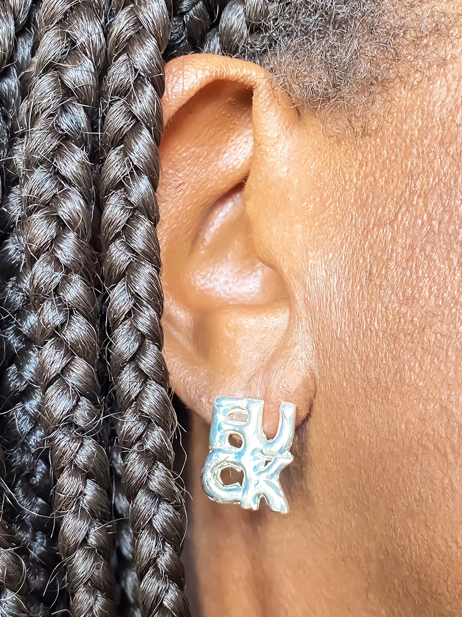 Close-up of silver ‘FUCK’ earring worn on right ear