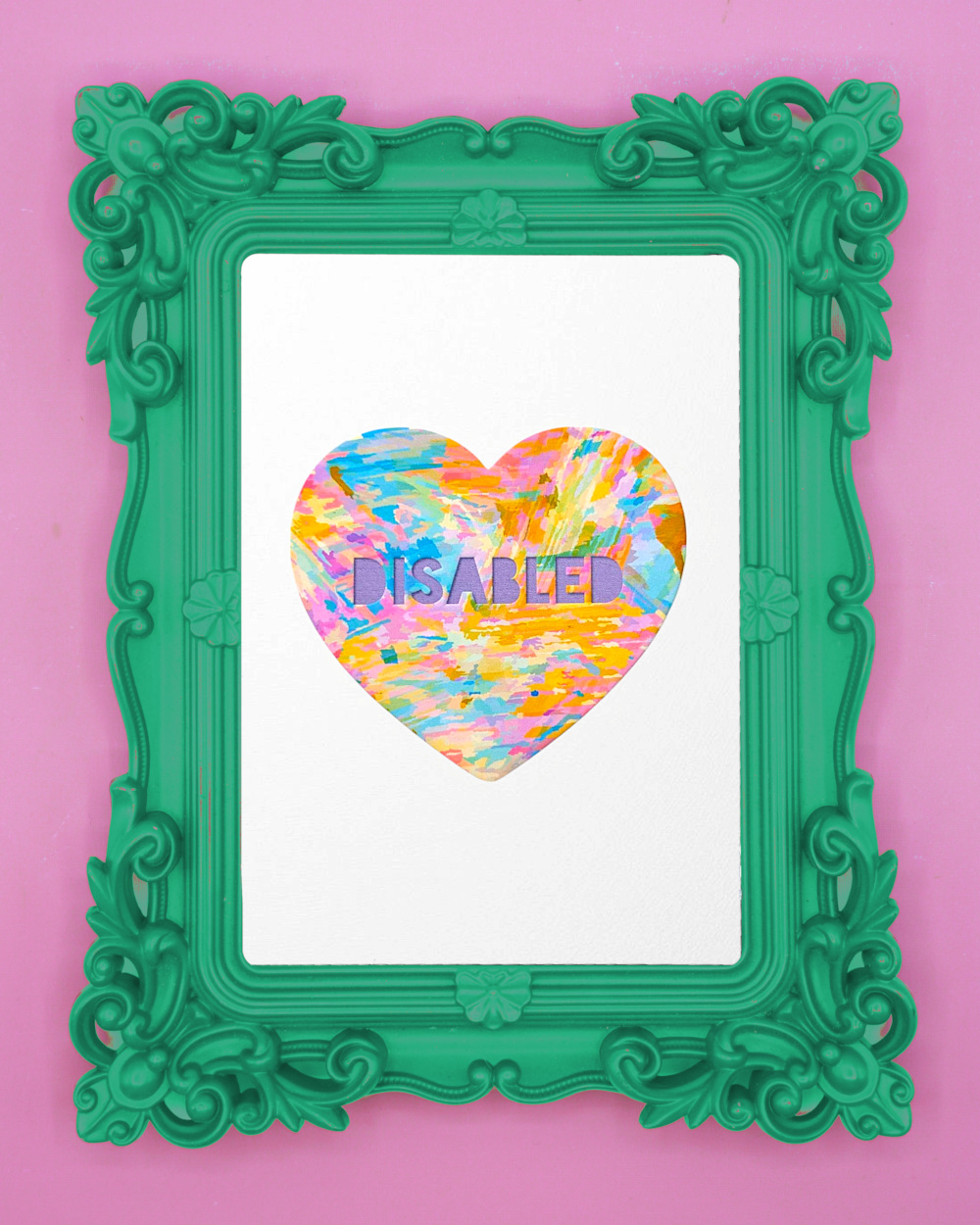 An art print featuring a heart with the word "DISABLED" in capital letters. The heart is filled with colourful, painterly textures. It’s framed in a playful ornate green frame against a soft pink background.