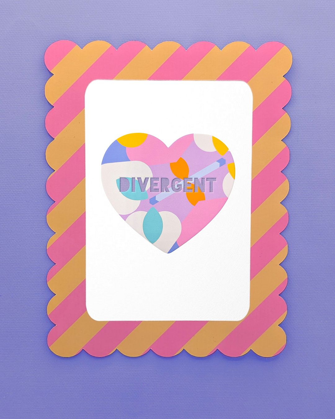 A colourful framed art print featuring a heart with the word "DIVERGENT" in block letters. The heart has a bold, abstract pattern in pink, purple, yellow, and blue. The frame is scalloped with alternating diagonal stripes of pink and gold on a purple background.